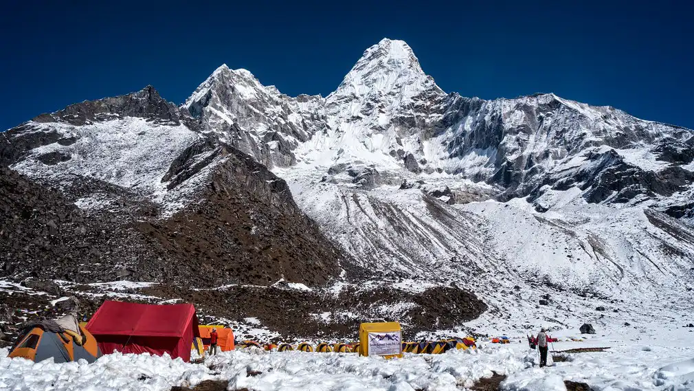 Ama Dablam Base Camp with colorful tents set up against the backdrop of the snow-covered Ama Dablam peak under a clear blue sky.