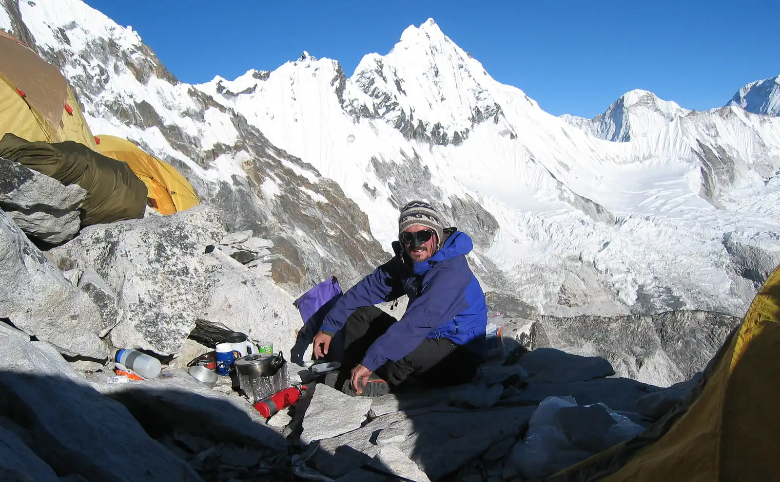 Climber resting at Camp 1 of Ama Dablam Expedition with snow-covered peaks in the background.