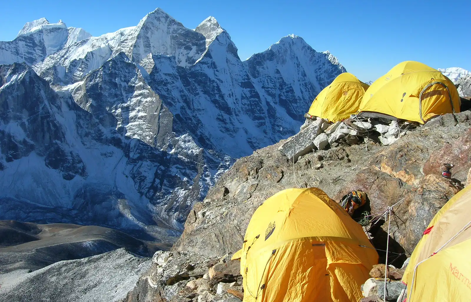 Yellow tents at Camp 2 of the Ama Dablam Expedition, perched on a rocky ledge with towering snow-capped peaks in the background.