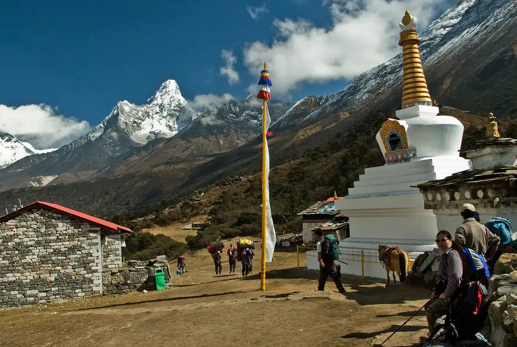 Trekkers arriving at Tengboche with Ama Dablam towering in the background and a white stupa nearby.