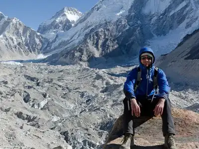 A trekker sits above the Khumbu Glacier, with snow-covered mountains in the background.