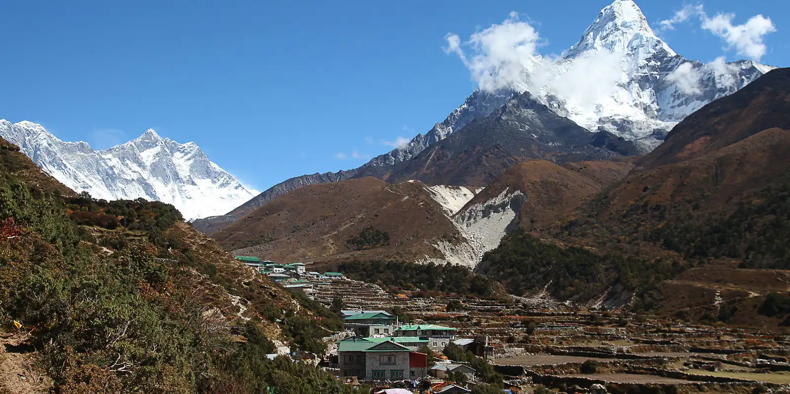 Ama Dablam mountain towering over Pangboche village in the Everest region of Nepal, with terraced fields and traditional houses in the foreground.