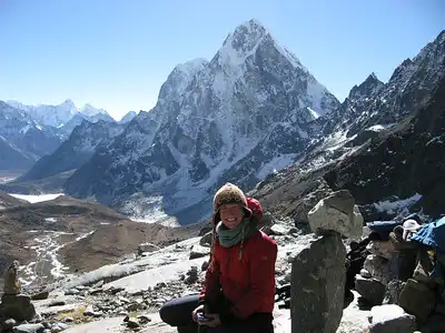 Female trekker sitting at Chola Pass with a backdrop of towering snow-capped peaks and a clear blue sky.