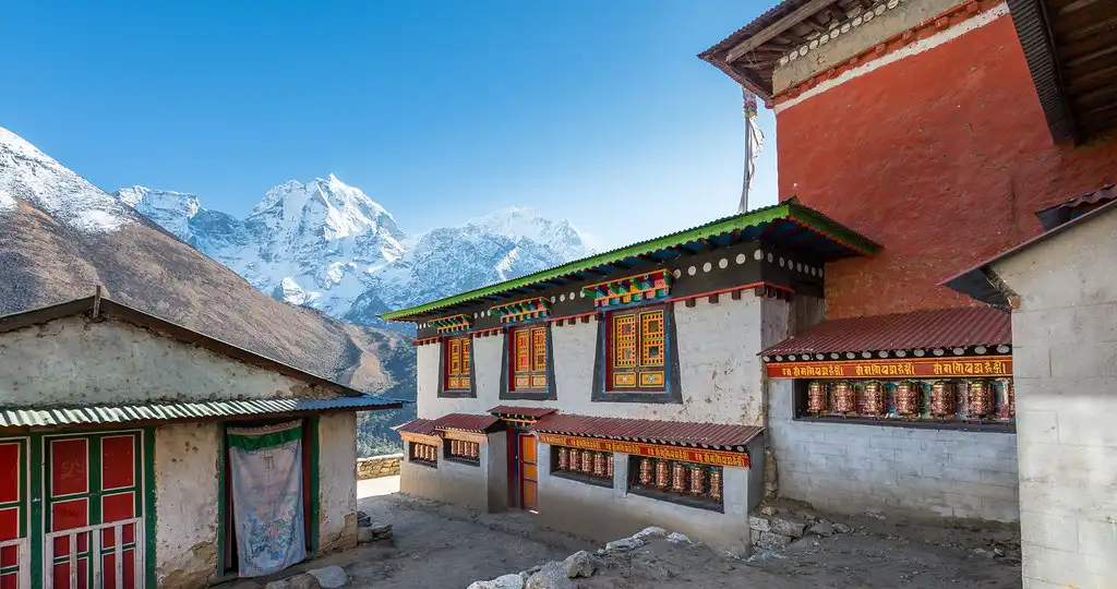 Traditional Buddhist monastery in Pangboche with colorful prayer wheels and a backdrop of snow-capped Himalayan peaks.