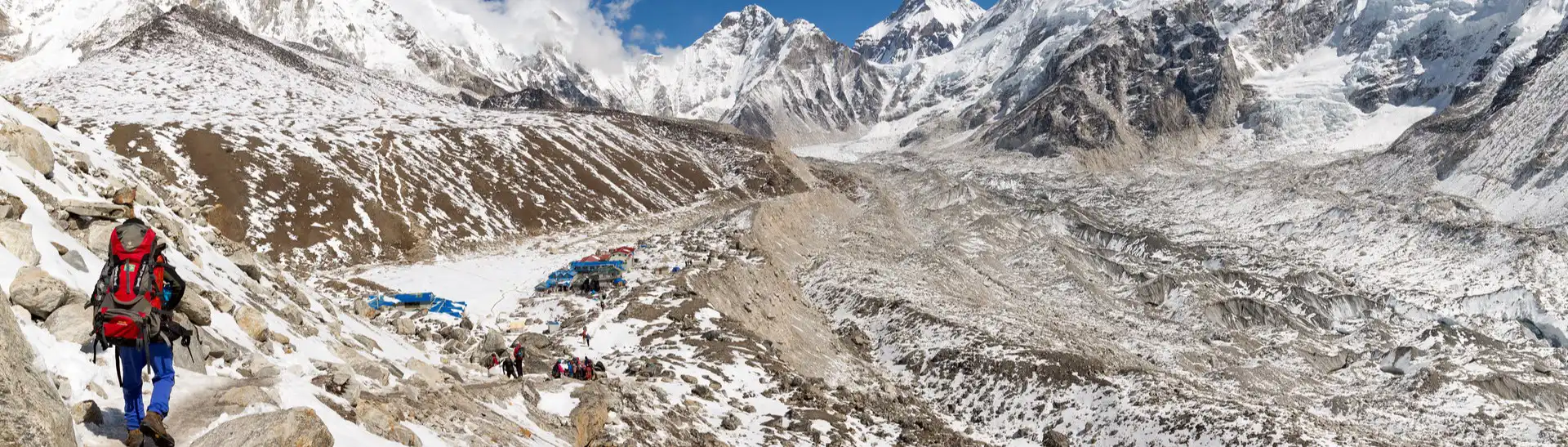 A trekker approaches the remote village of Gorakshep, nestled in the snowy, rugged terrain of the Himalayas, surrounded by towering peaks under a clear blue sky.