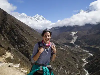 A female trekker smiling as she heads towards Pangboche village with the Himalayan mountains in the background.