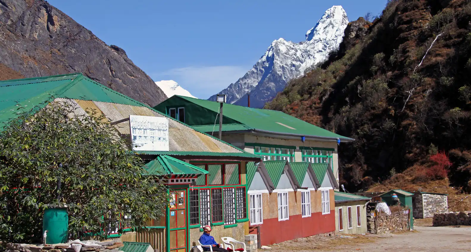 Buildings with green roofs in Khumjung village, Nepal, with snow-capped mountains in the background.