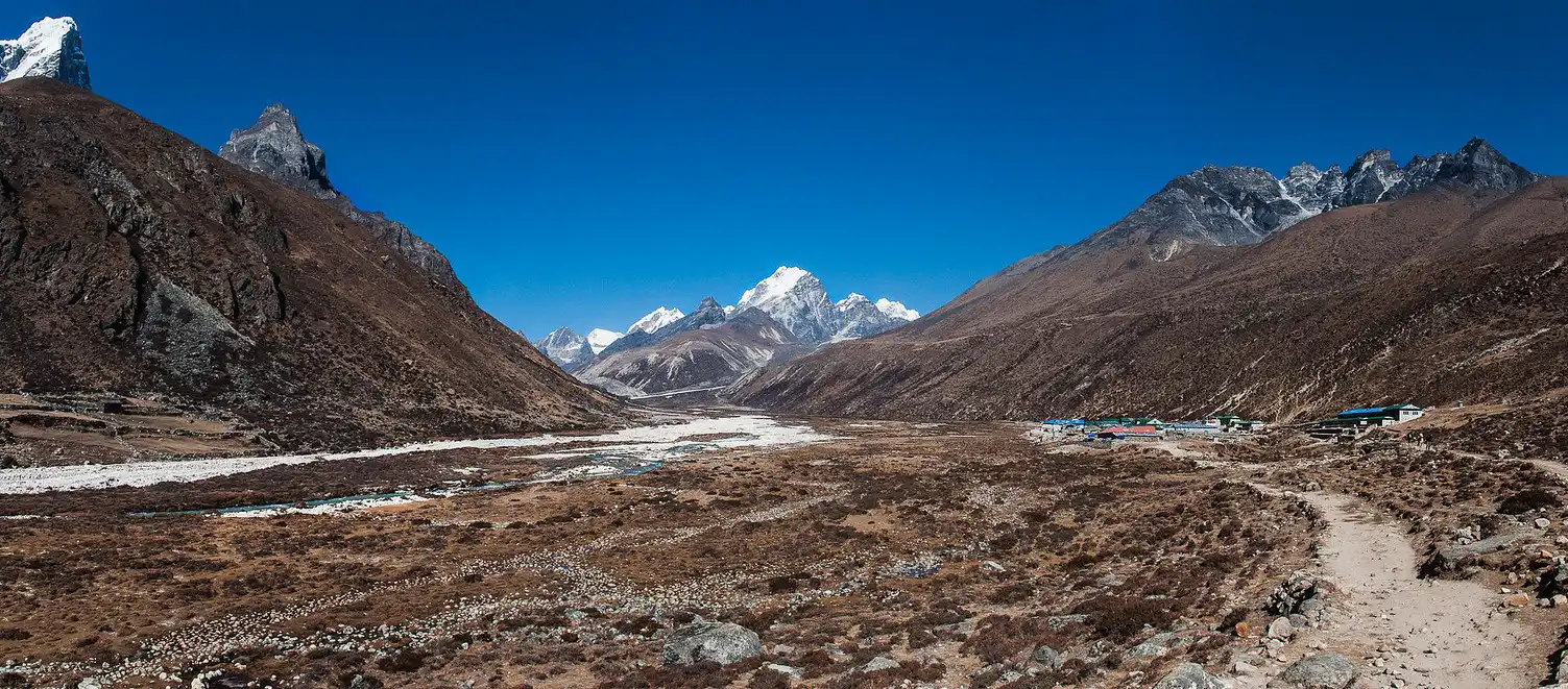 A panoramic view of the trail leading to Lobuche East Peak, with snow-capped mountains in the distance and a wide, barren valley below.