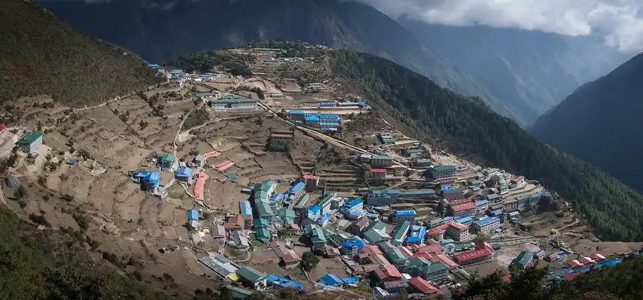 Aerial view of Namche Bazaar, a vibrant mountain town with colorful buildings nestled in a natural amphitheater surrounded by the Himalayas.