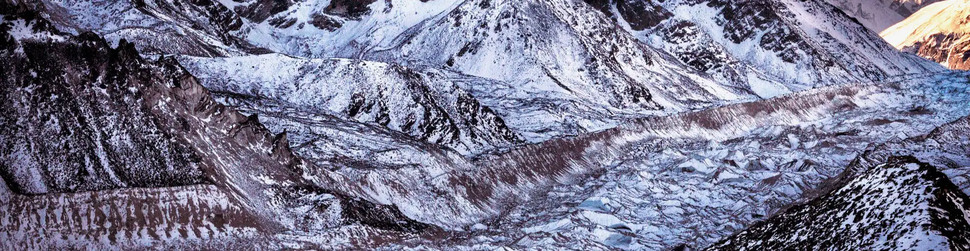 Panoramic view of the Khumbu Glacier with its intricate ice formations and surrounding rugged mountains under a twilight sky.