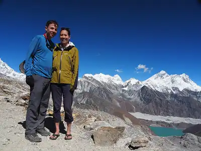 Two hikers standing together at Renjo La Pass with the dramatic backdrop of the Himalayan mountain range and a turquoise glacial lake.