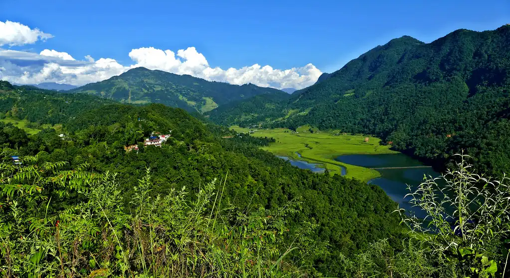 Panoramic view of Rupa Lake surrounded by lush green mountains under a clear blue sky in Nepal