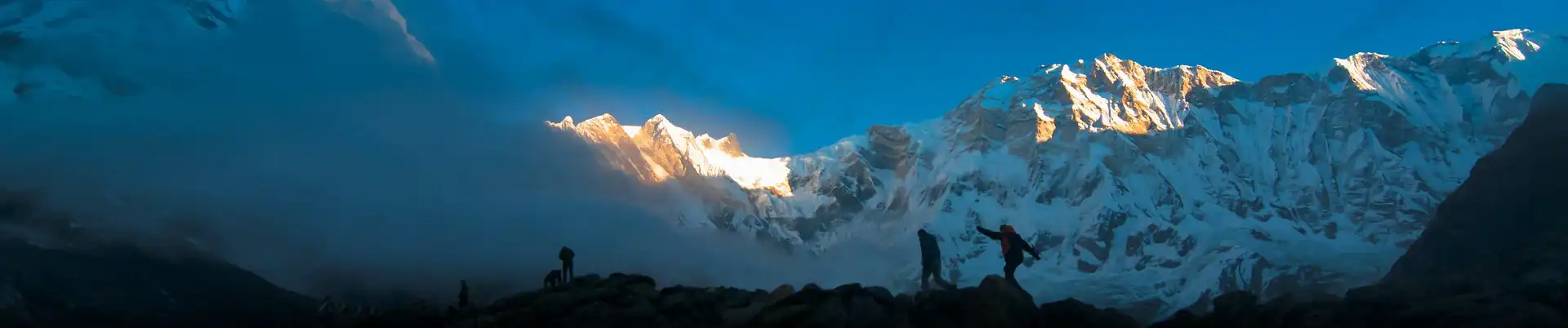 Two trekkers silhouetted against a backdrop of snow-capped mountains as the first rays of the sun illuminate Annapurna Base Camp.