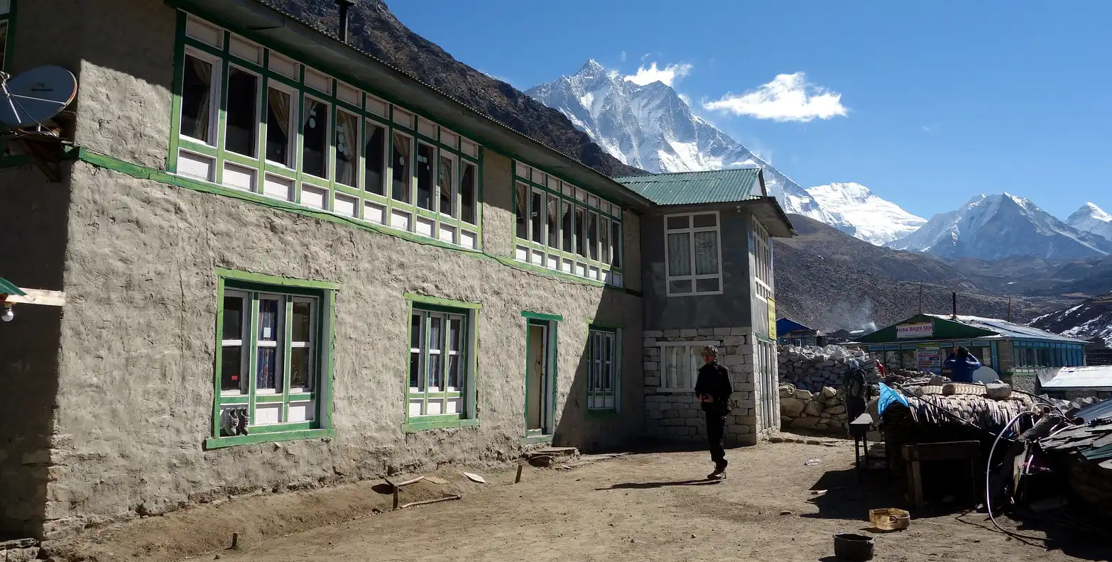 The Mountain Paradise Lodge in Dingboche, with traditional architecture, set against a backdrop of snow-capped Himalayan peaks under a clear blue sky.