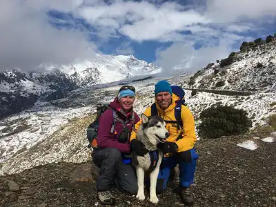 Trekkers with a dog in the snowy Khumbu Region, Nepal, with mountain scenery in the background.