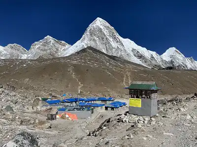 A clear view from Gorakshep, showcasing the village with its blue-roofed buildings against the backdrop of towering, snow-covered Himalayan peaks under a deep blue sky.