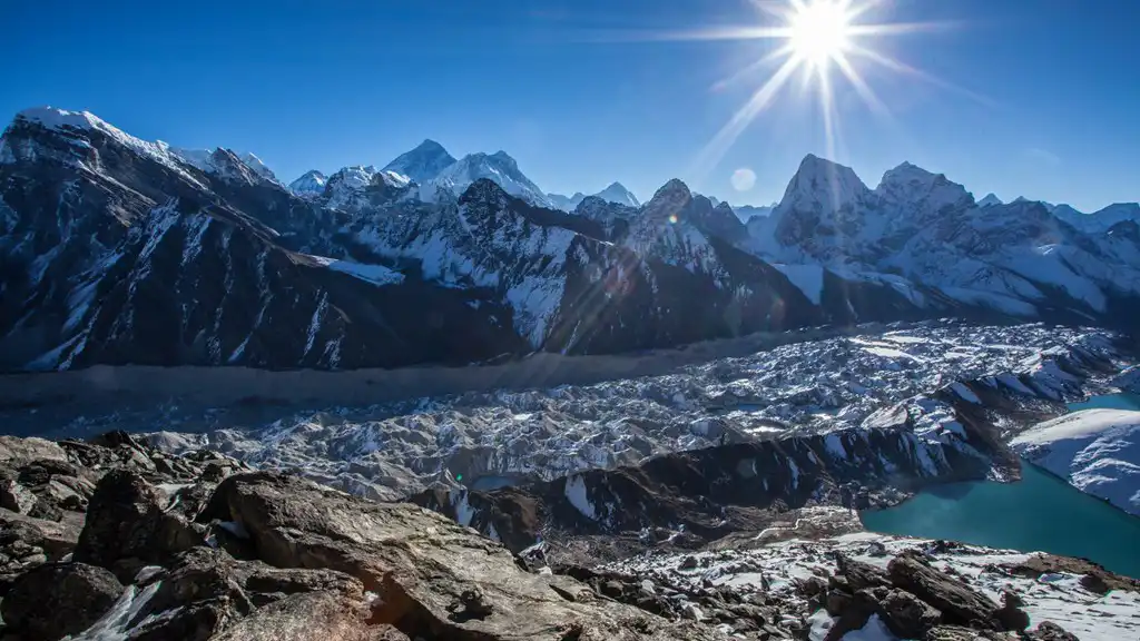 Sunburst over the Himalayas, with a clear view from Kala Patthar featuring snowy mountains, a glacier, and a turquoise lake.