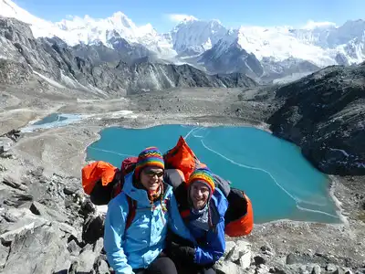 Two trekkers at the top of Kongma La Pass with a view of a turquoise lake and snow-capped mountains