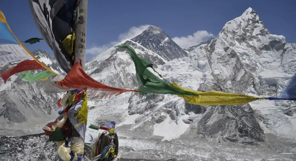 Colorful prayer flags flutter in the wind with a stunning view of Mount Everest and surrounding snow-covered peaks from Kala Patthar.