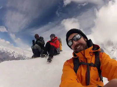 Group of climbers taking a photo at the summit of Island Peak with snowy peaks and clouds in the background