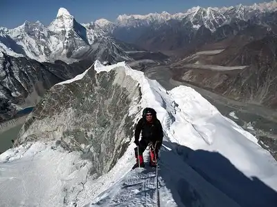 A climber traversing the narrow snow-covered ridge on Island Peak with majestic Himalayan peaks in the background.