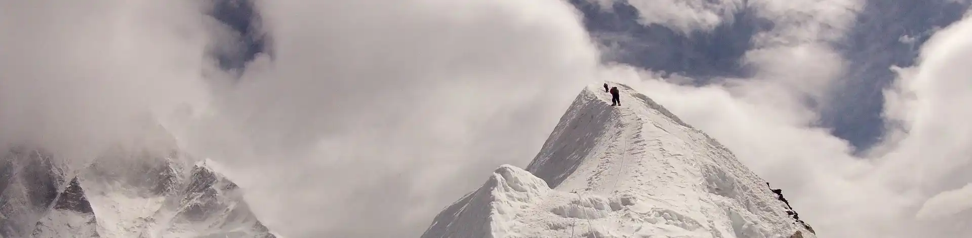 Climbers approaching the summit of snow-covered Island Peak under partly cloudy skies