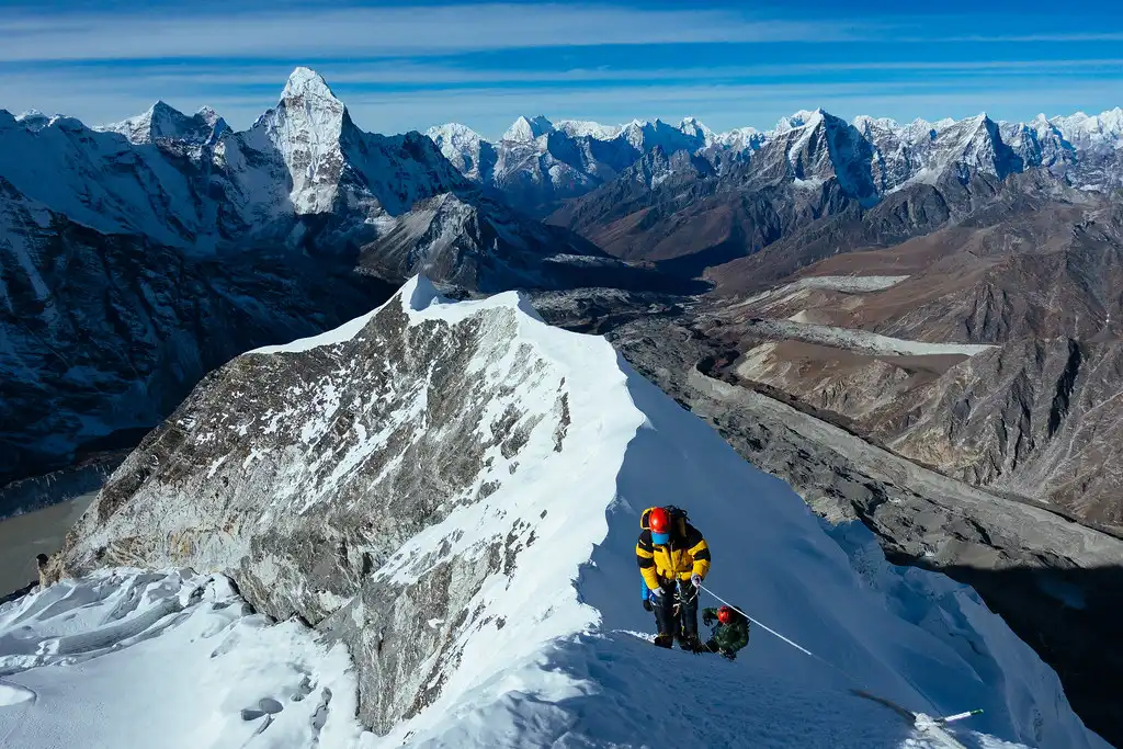 Climbers ascending a steep snow-covered ridge toward the summit of Island Peak with a panoramic view of snow-capped mountains in the background