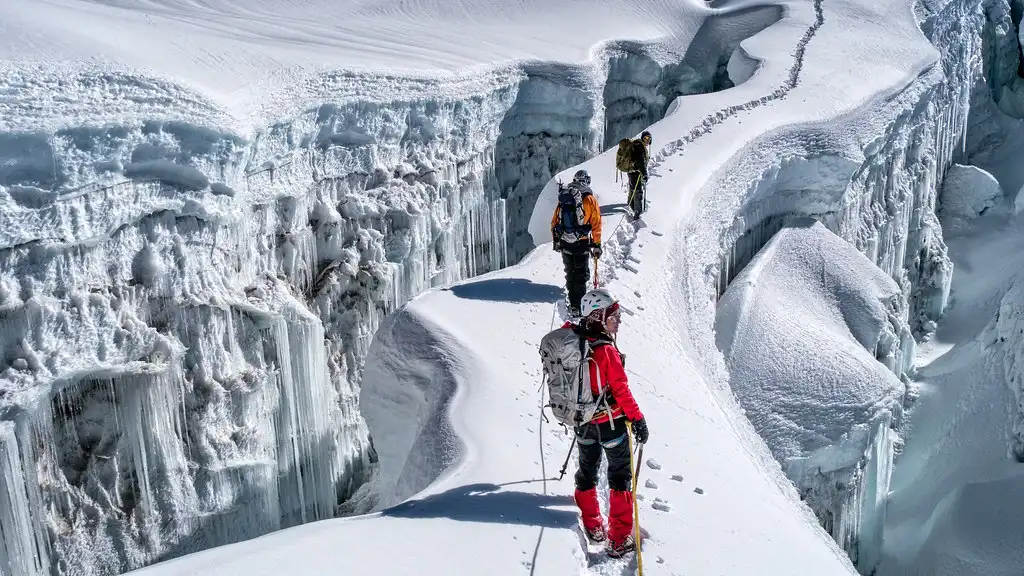 Climbers ascending a snowy ridge on Island Peak with deep crevasses and icy terrain around them.