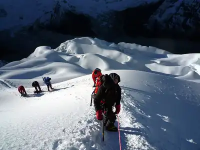 A group of climbers in red and black gear roped together, ascending a snowy slope on Island Peak.