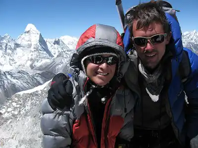 Two climbers in winter gear on the summit of Island Peak with snowy mountain peaks in the background.