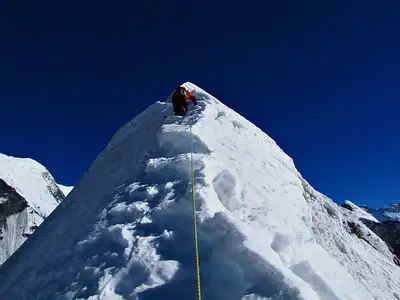 Climber ascending a narrow snow-covered ridge on Island Peak under a clear blue sky.