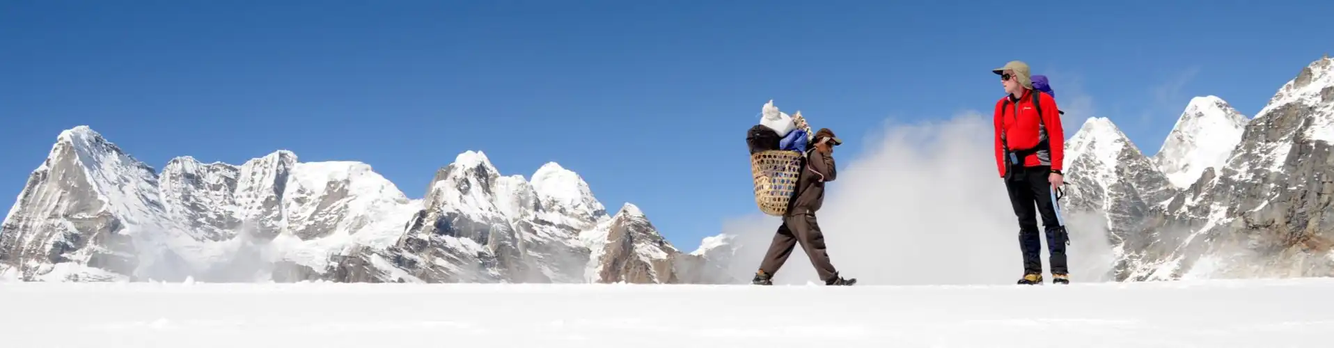 A climber and a porter crossing the snowy terrain of Mera Peak with towering snow-capped mountains in the background.