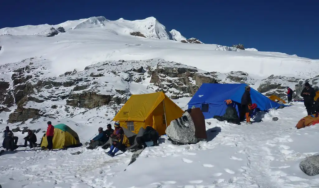 Tents set up at Mera Peak Base Camp, surrounded by snow-covered terrain and towering mountains under a clear blue sky, with climbers preparing for their ascent.