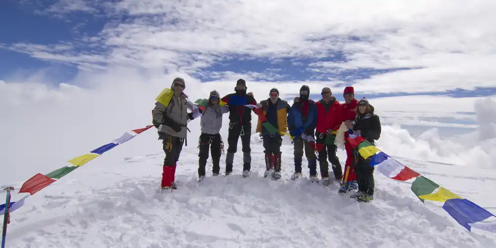 Group of climbers standing at Mera Peak summit with prayer flags, surrounded by snow and clouds.