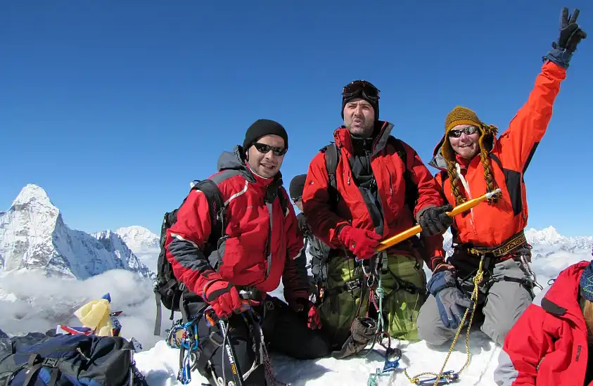 Climbers at the summit of Island Peak wearing red jackets, posing with ice axes against a backdrop of snow-covered mountains.