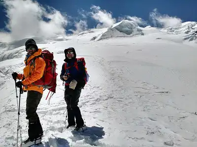 Two climbers on the snowy slopes of Mera Peak, standing with trekking poles, preparing to continue their ascent under a bright sky.